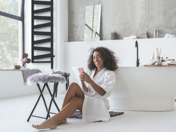 Smiling woman sitting in the bathroom on the floor with a smartphone in her hands