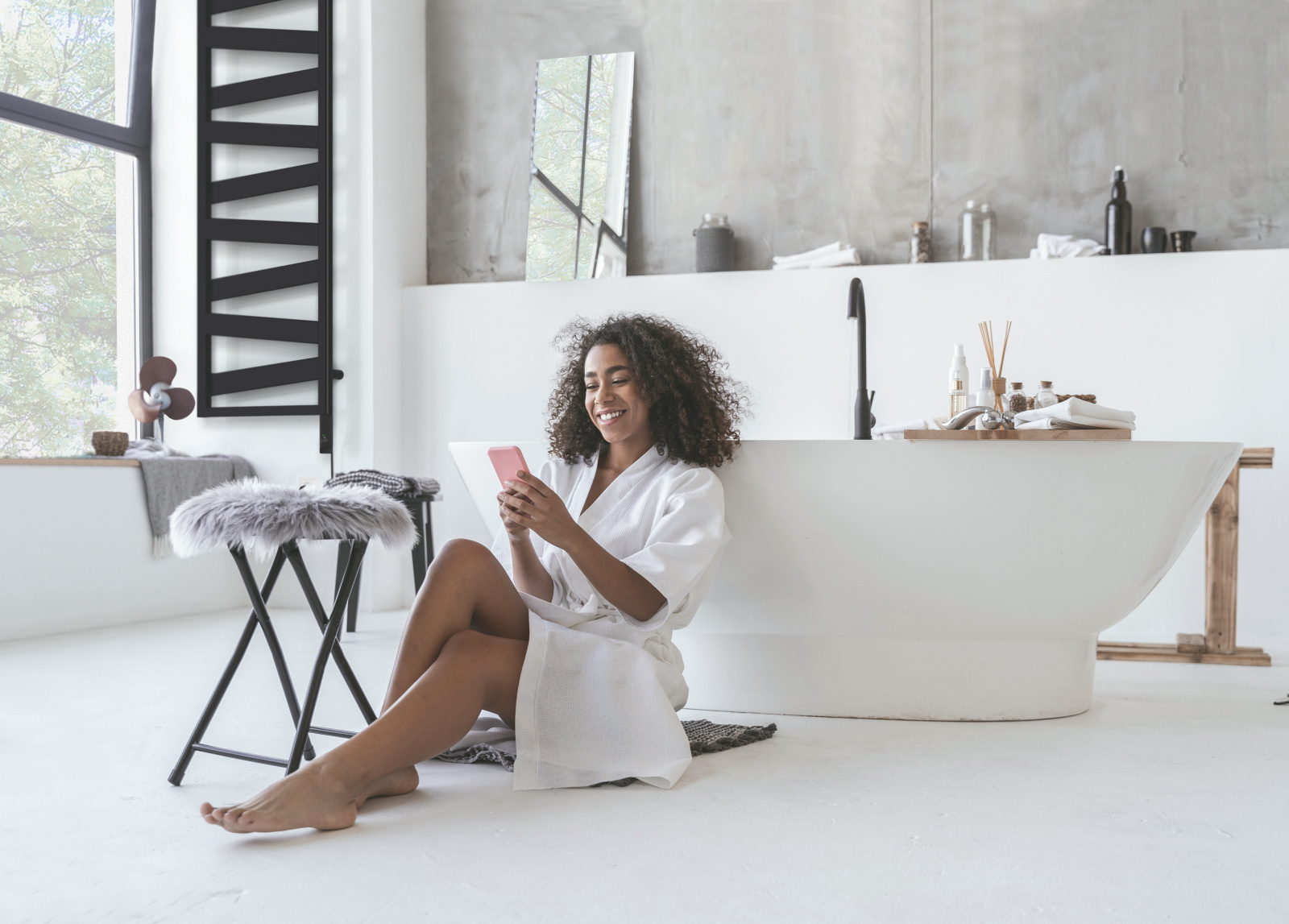Zehnder_RAD_Ribbon-EL_zeh-nih-keyvisual-300dpi-cmyk Smiling woman sitting in the bathroom on the floor with a smartphone in her hands